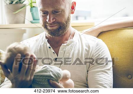 Portrait of father holding baby, sitting on sofa beside mother View Large Photo Image Picture - Portrait of father holding baby, sitting on sofa beside mother. Fotosearch