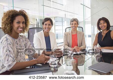 Stock Photo - Portrait of four cheerful women sitting at conference table. Fotosearch