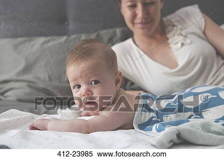 Portrait of little baby lying on bed with mother smiling in background View Large Photo Image Stock Photography - Portrait of little baby lying on bed with mother smiling in background. Fotosearch