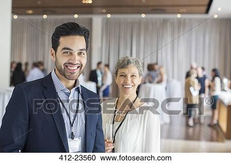 Stock Image - Portrait of man and woman standing in lobby of conference center smiling. Fotosearch