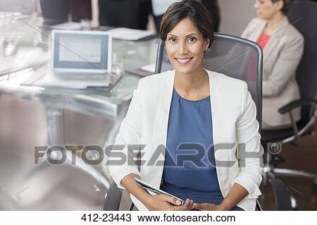 Stock Image - Portrait of smiling businesswoman posing with tablet pc in conference room. Fotosearch