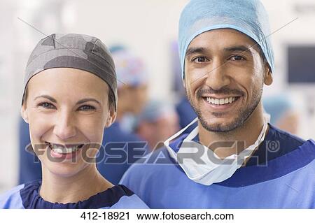 Stock Image - Portrait of smiling doctors wearing surgical caps in operating theater. Fotosearch