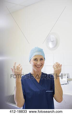 Stock Image - Portrait of smiling female doctor wearing surgical cap and gown in hospital. Fotosearch