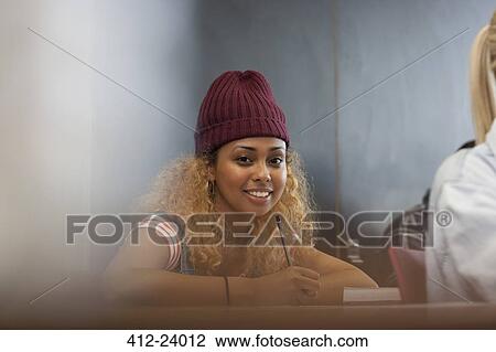 Stock Image - Portrait of smiling female university student writing down notes in classroom. Fotosearch