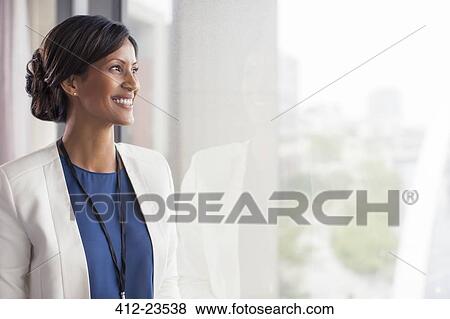 Stock Photo - Portrait of smiling mid adult woman looking through window. Fotosearch