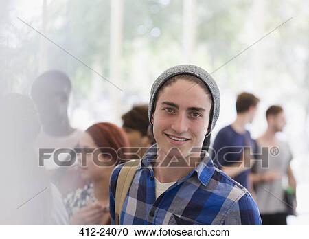 Stock Image - Portrait of smiling university student during break, people talking in background. Fotosearch