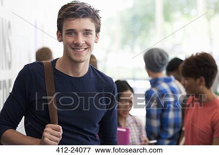 Stock Photo - Portrait of smiling university student standing in corridor during break, people in background talking. Fotosearch
