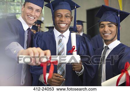 Stock Image - Portrait of smiling university students holding diplomas after graduation ceremony. Fotosearch
