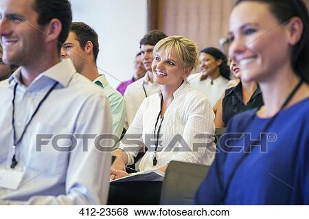 Stock Photo - Portrait of smiling woman sitting in conference room, with man and woman in blurred foreground. Fotosearch