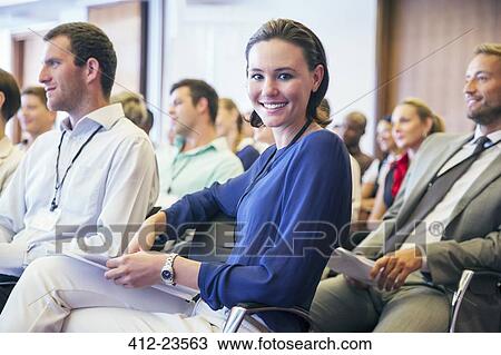 Stock Image - Portrait of smiling young woman sitting in audience in conference room. Fotosearch