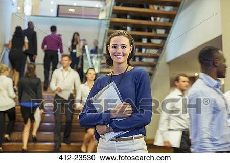 Portrait of smiling young woman standing in lobby of conference center View Large Photo Image Stock Image - Portrait of smiling young woman standing in lobby of conference center. Fotosearch