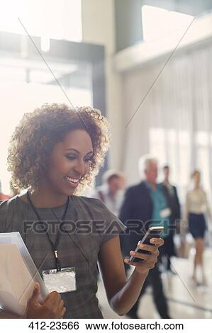 Portrait of smiling young woman standing in lobby of conference center, using smartphone View Large Photo Image Stock Photograph - Portrait of smiling young woman standing in lobby of conference center, using smartphone. Fotosearch