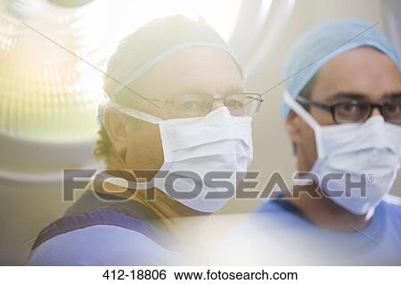 Stock Photograph - Portrait of two doctors wearing surgical caps, masks and glasses in operating theater. Fotosearch