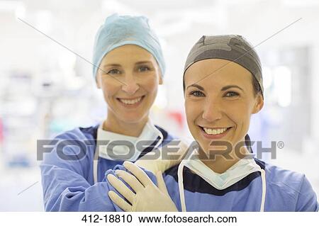 Stock Image - Portrait of two smiling female doctors wearing surgical caps in operating theater. Fotosearch