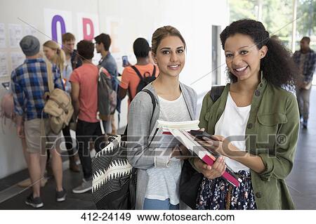 Portrait of two smiling female students holding books, other students in background View Large Photo Image Stock Photo - Portrait of two smiling female students holding books, other students in background. Fotosearch