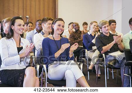 Picture - Portrait of two smiling women sitting in among other conference participants in conference room, applauding. Fotosearch