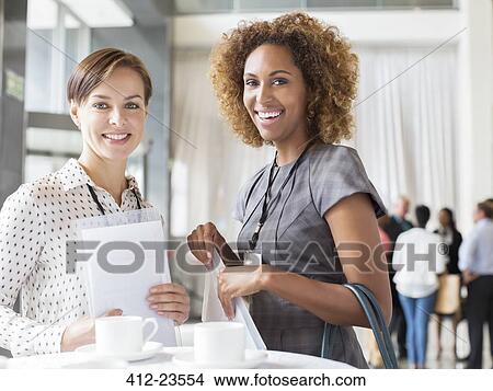 Portrait of two smiling women standing in lobby of conference center during coffee break View Large Photo Image Picture - Portrait of two smiling women standing in lobby of conference center during coffee break. Fotosearch
