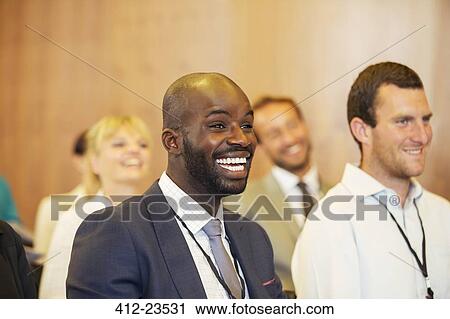 Stock Image - Portrait of two young men, one laughing, sitting in conference room. Fotosearch
