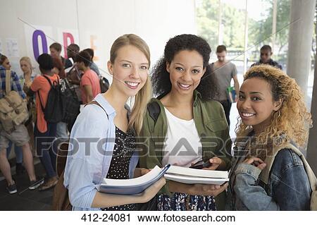Stock Image - Portrait of university friends standing in corridor with books. Fotosearch