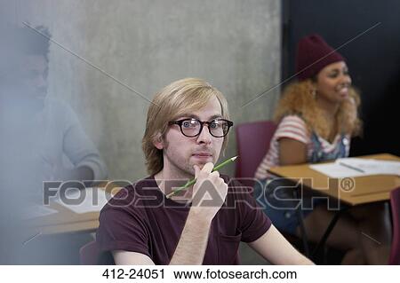 Stock Image - Portrait of university student sitting at desk with hand on chin. Fotosearch