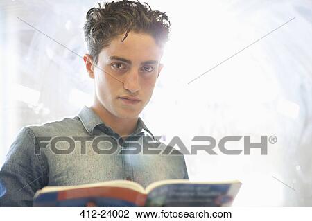 Stock Image - Portrait of university student with book standing beside window. Fotosearch