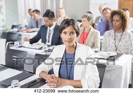 Stock Photo - Portrait of woman with group of business people in background attending seminar. Fotosearch