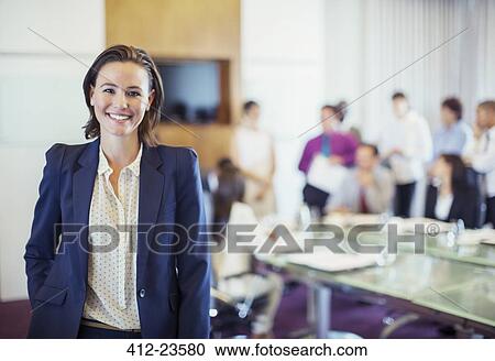 Portrait of young businesswoman smiling in conference room, people in background View Large Photo Image Stock Image - Portrait of young businesswoman smiling in conference room, people in background. Fotosearch