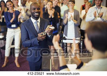 Portrait of young man holding trophy, standing in conference room, smiling to applauding audience View Large Photo Image Stock Image - Portrait of young man holding trophy, standing in conference room, smiling to applauding audience. Fotosearch
