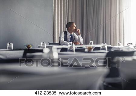 Stock Photography - Portrait of young man sitting at table in empty conference room looking through window. Fotosearch