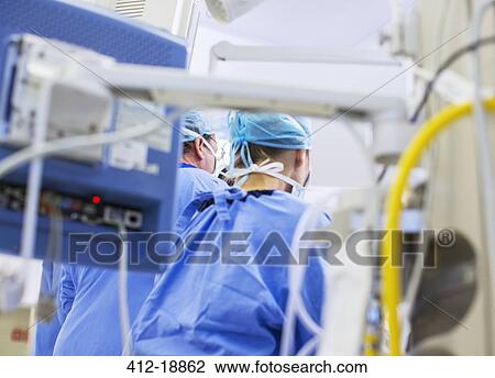 Stock Image - Rear view of doctors in operating theater, medical equipment in foreground. Fotosearch
