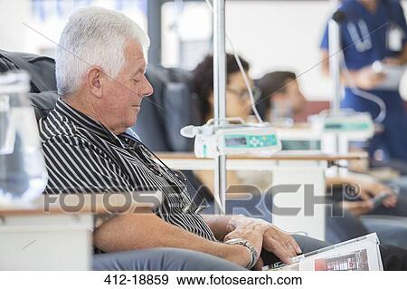 Stock Photo - Senior man reading magazine undergoing medical treatment in outpatient clinic. Fotosearch