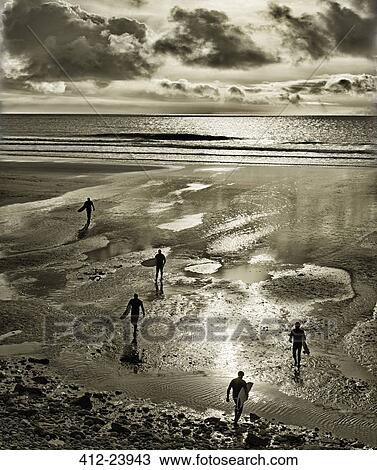 Stock Image - Silhouettes of surfers walking with surfboards on Perranuthnoe Beach. Fotosearch