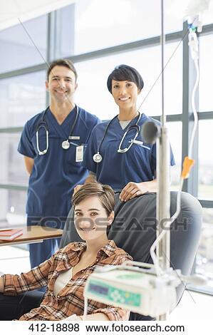 Stock Photo - Smiling doctors standing by patient undergoing medical treatment in outpatient clinic. Fotosearch