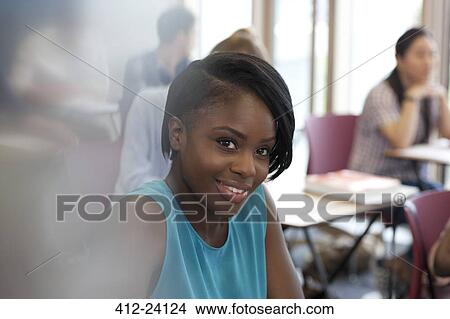 Picture - Smiling female student during lecture looking at camera with other students in background. Fotosearch