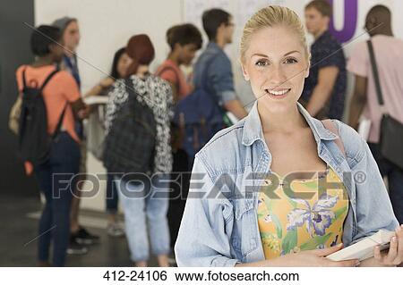 Smiling female student holding books other students in background View Large Photo Image Stock Photograph - Smiling female student holding books other students in background. Fotosearch