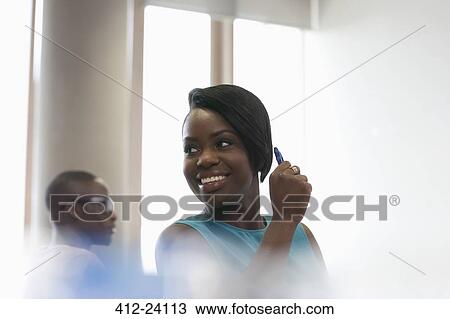Stock Image - Smiling female student looking away in sunlit classroom. Fotosearch