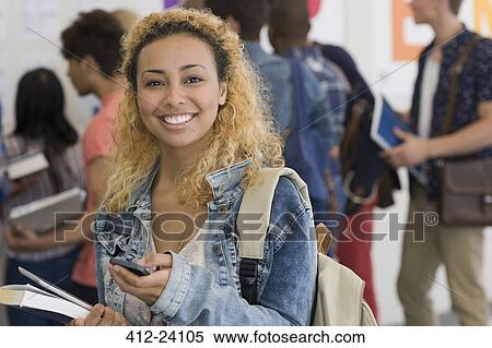 Stock Photography - Smiling female student using cell phone with other students in background. Fotosearch