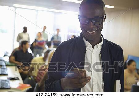 Smiling male student in eyeglasses looking at smart phone, with other students in background View Large Photo Image Stock Photo - Smiling male student in eyeglasses looking at smart phone, with other students in background. Fotosearch