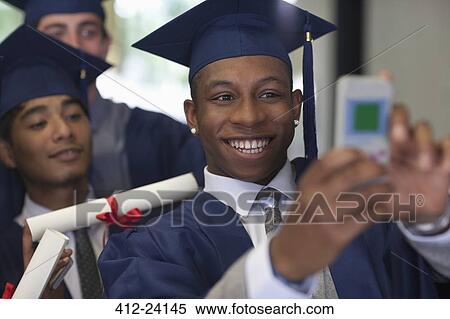 Smiling male student wearing graduation clothes taking selfie with friends View Large Photo Image Stock Photography - Smiling male student wearing graduation clothes taking selfie with friends. Fotosearch