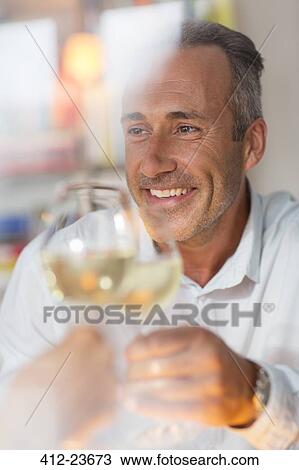 Stock Image - Smiling older man toasting with white wine. Fotosearch