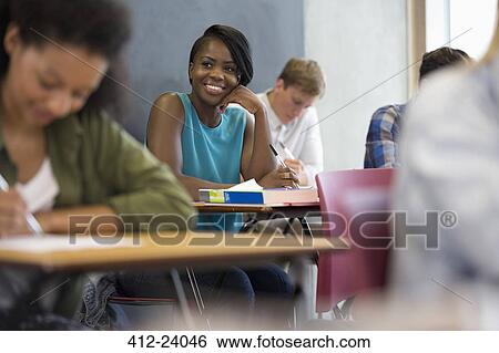 Smiling university student sitting at desk with hand on chin View Large Photo Image Stock Photograph - Smiling university student sitting at desk with hand on chin. Fotosearch