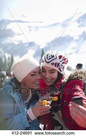 Stock Image - Smiling women in warm clothing drinking tea outdoors. Fotosearch