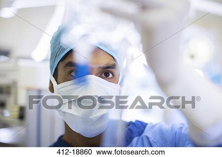 Surgeon wearing surgical mask, cap and gloves looking closely at IV drip View Large Photo Image Stock Image - Surgeon wearing surgical mask, cap and gloves looking closely at IV drip. Fotosearch