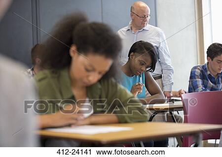 Teacher walking along desks and checking students during test View Large Photo Image Stock Image - Teacher walking along desks and checking students during test. Fotosearch