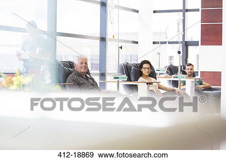 Stock Photo - Three patients sitting in armchairs, undergoing medical treatment in outpatient clinic. Fotosearch