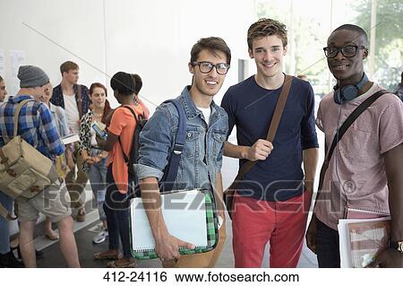 Three smiling male students standing together with other students in background View Large Photo Image Stock Photograph - Three smiling male students standing together with other students in background. Fotosearch