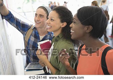 Three smiling students looking at information board, holding books and digital tablet View Large Photo Image Stock Photograph - Three smiling students looking at information board, holding books and digital tablet. Fotosearch