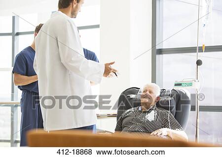 Stock Photo - Two doctors talking to senior patient undergoing medical treatment in outpatient clinic. Fotosearch