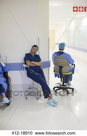 Stock Image - Two doctors wearing surgical clothing resting in hospital corridor. Fotosearch