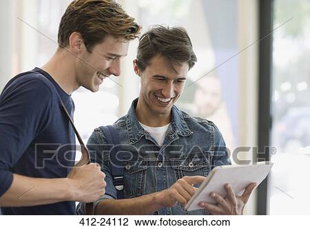 Stock Image - Two male students looking at digital tablet and laughing. Fotosearch